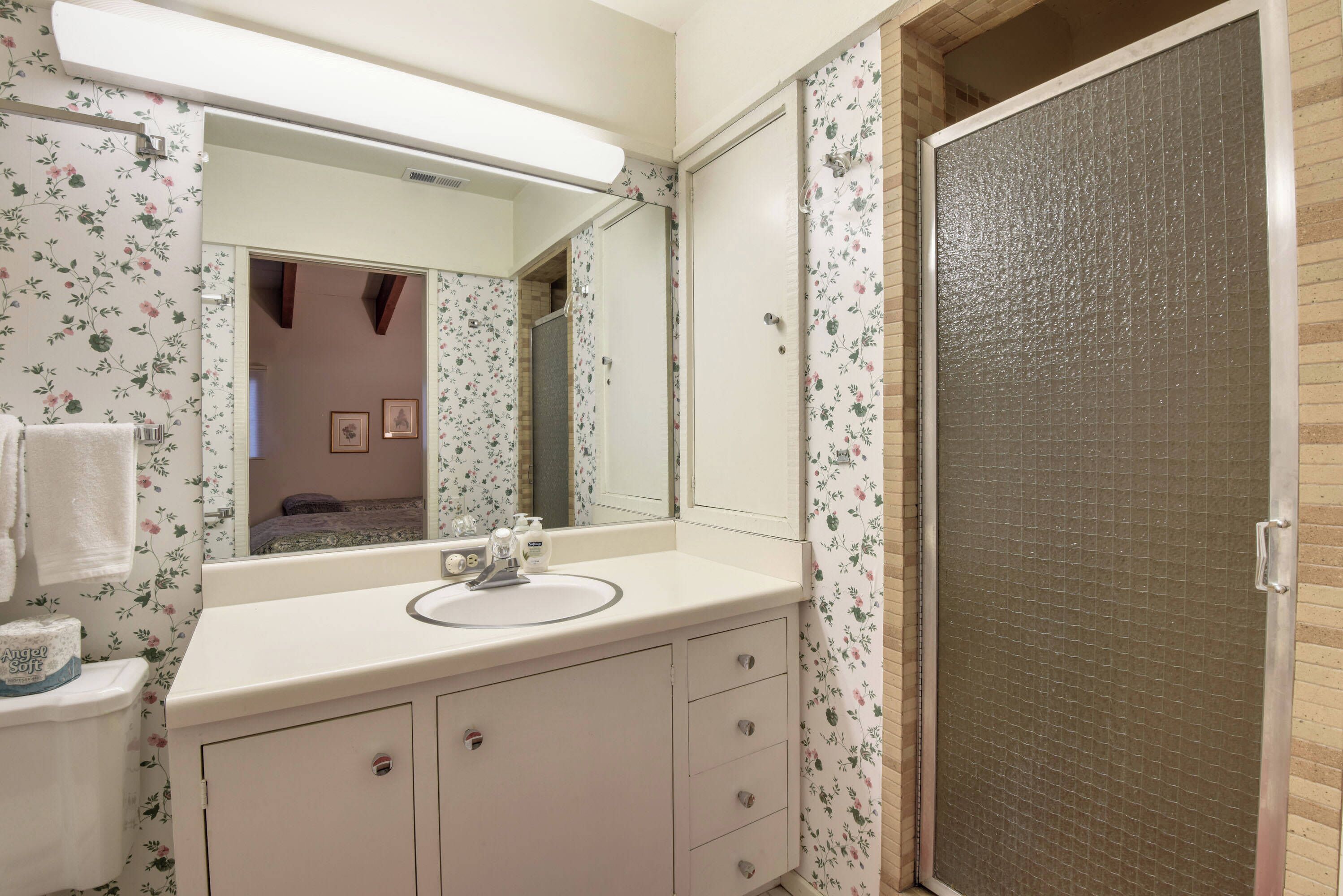A bathroom with a white sink, mirror, and floral wallpaper.