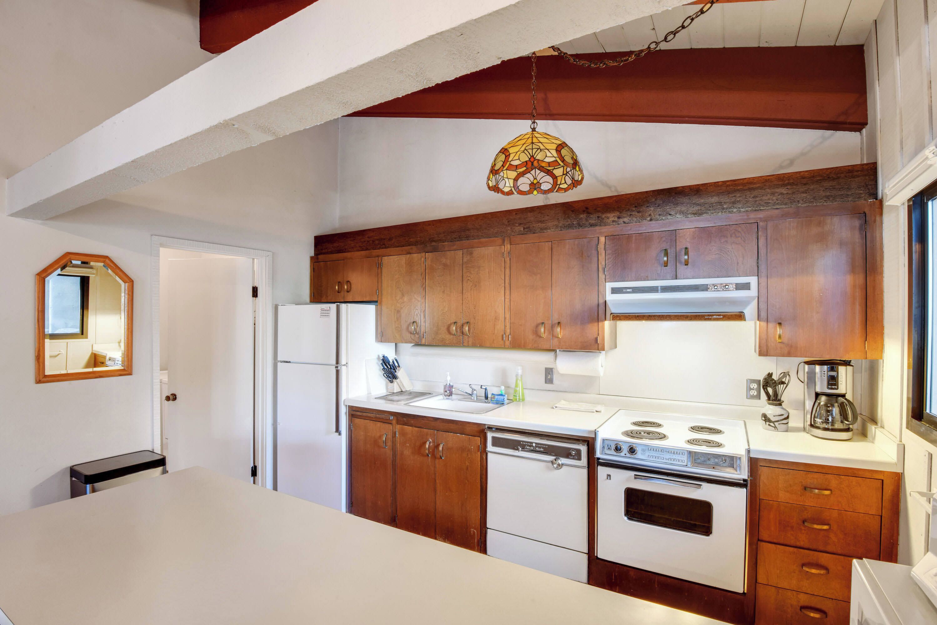 A kitchen with wooden cabinets, a white countertop, a stove, a dishwasher, and a hanging light fixture.