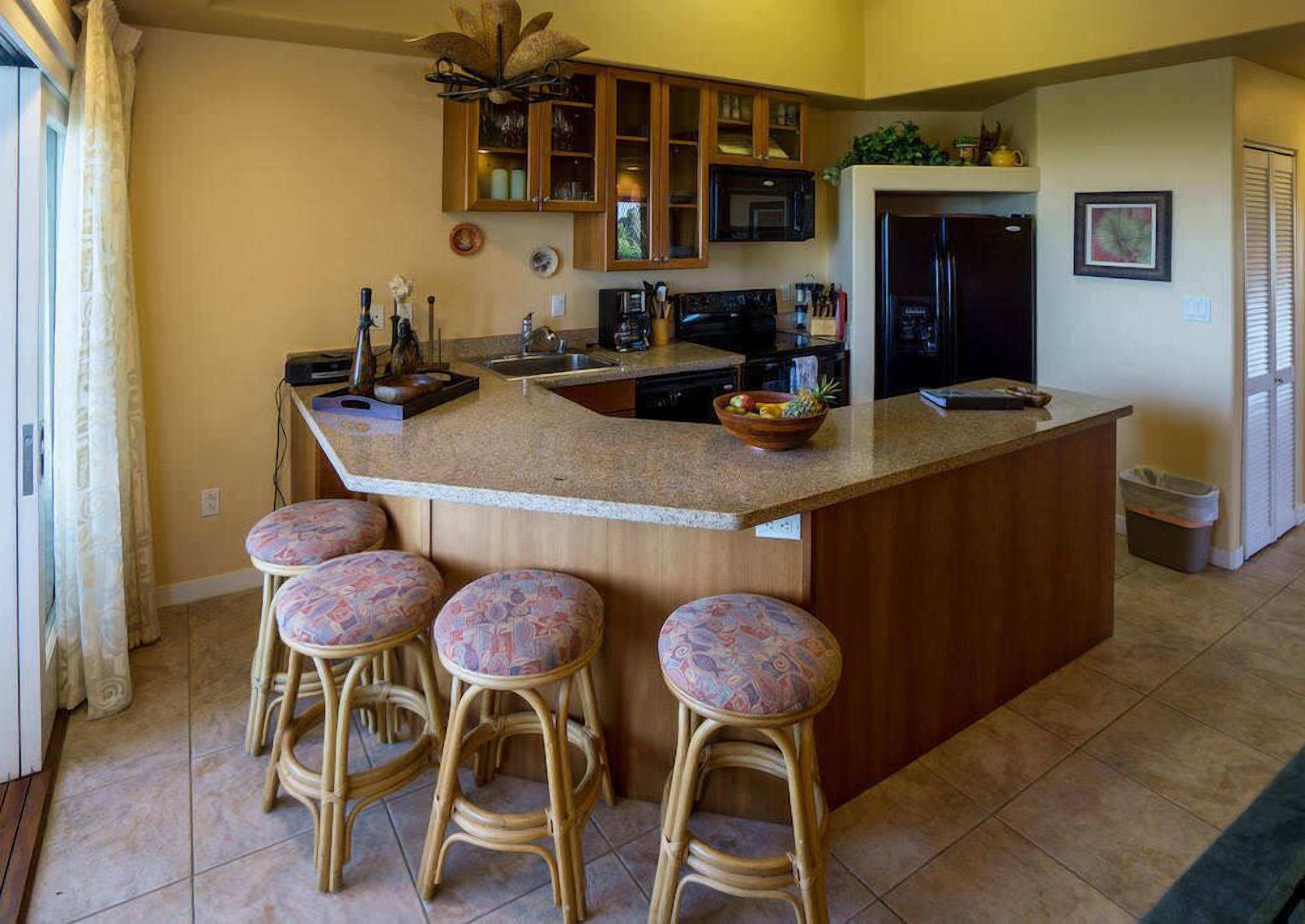Una cocina con una isla central, taburetes de bar, armarios de madera, un microondas y un refrigerador.