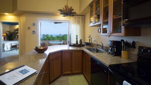 A kitchen with wooden cabinets, a black stove, a coffee maker, and a view of the outdoors. - The Beach Villas w/ Pool Hot Tub & A/c! (Kailua-Kona)