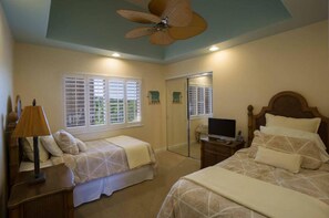 A bedroom with two beds, a ceiling fan, a TV on a stand, and a window with shutters. - The Beach Villas w/ Pool Hot Tub & A/c! (Kailua-Kona)