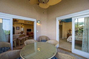 A dining area with a round glass table and wicker chairs, a kitchen in the background, and a bedroom visible through a glass door. - The Beach Villas w/ Pool Hot Tub & A/c! (Kailua-Kona)