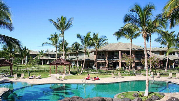 Un resort con una piscina grande rodeada de palmeras y un edificio con varios balcones.