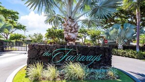 Un letrero de piedra con la inscripción "the Fairways", rodeado de plantas tropicales y palmeras.