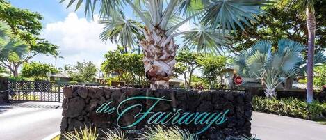 A stone sign with "the Fairways" written on it, surrounded by tropical plants and palm trees.