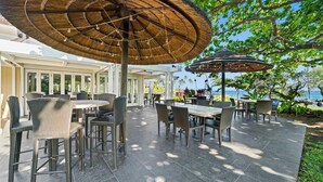 Un patio al aire libre con mobiliario de mimbre y sombrillas de paja, con vistas a un paisaje pintoresco.