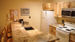 A kitchen with a granite countertop, a refrigerator, a microwave, and wooden cabinets. - Well-appointed Condo Near Chairlifts (Whitefish)