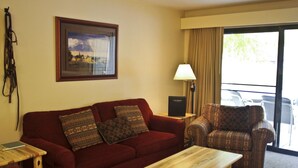 A living room with a red sofa, patterned cushions, a wooden coffee table, a patterned armchair, a framed picture on the wall, and a lamp. - Well-appointed Condo Near Chairlifts (Whitefish)