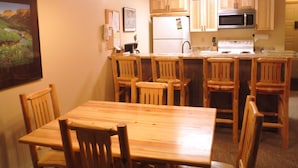A compact kitchen with wooden cabinets, a refrigerator, a microwave, and a stove. There is a wooden dining table with chairs. - Well-appointed Condo Near Chairlifts (Whitefish)