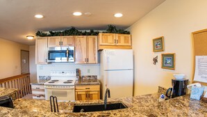 Une cuisine avec des meubles en bois, un réfrigérateur blanc, une cuisinière, un four à micro-ondes et des plans de travail en granit.