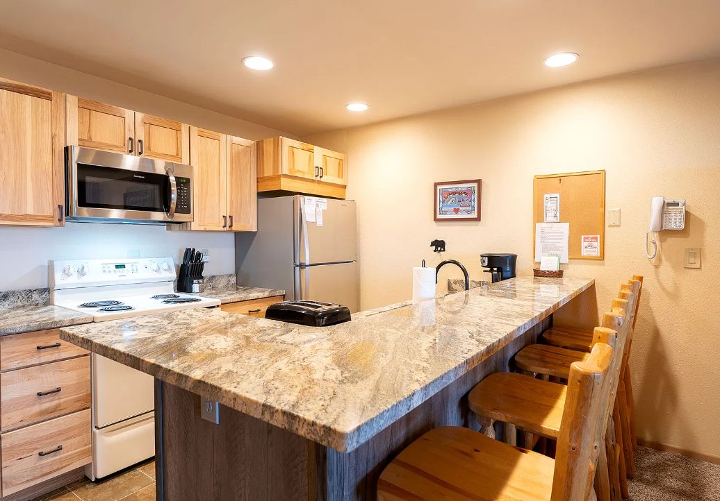 A kitchen with wooden cabinets, a stainless steel microwave, a refrigerator, a stove, and a marble countertop.