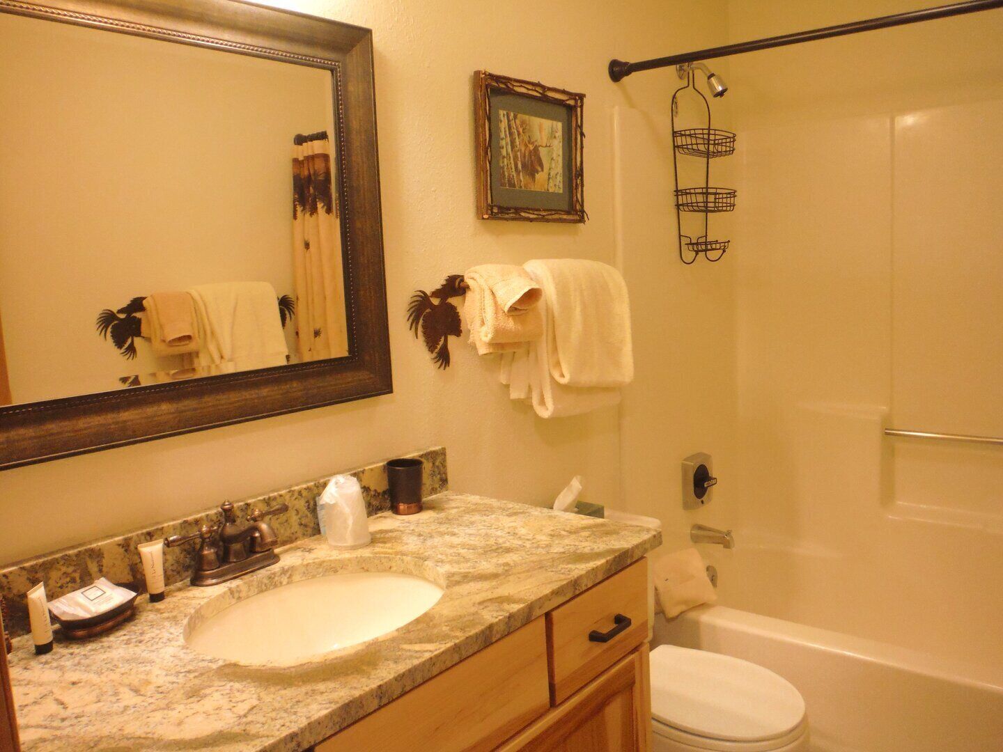 A bathroom with a marble sink, a large mirror, a framed picture, a towel rack, and a shower curtain rod.