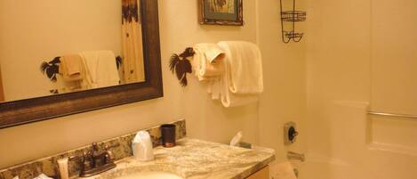 A bathroom with a marble sink, a large mirror, a framed picture, a towel rack, and a shower curtain rod.
