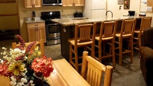 A kitchen with wooden cabinets, a microwave, a stove, a refrigerator, and a dining area with wooden chairs and a table. - Nicely Furnished Condo with Valley Views (Whitefish)