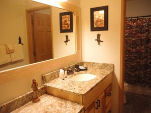 Une salle de bain avec un lavabo en marbre, des meubles en bois, un grand miroir et un rideau de douche à motifs floraux.