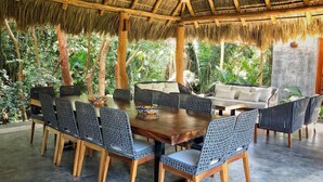 A dining area with a wooden table and wicker chairs, surrounded by lush greenery.
