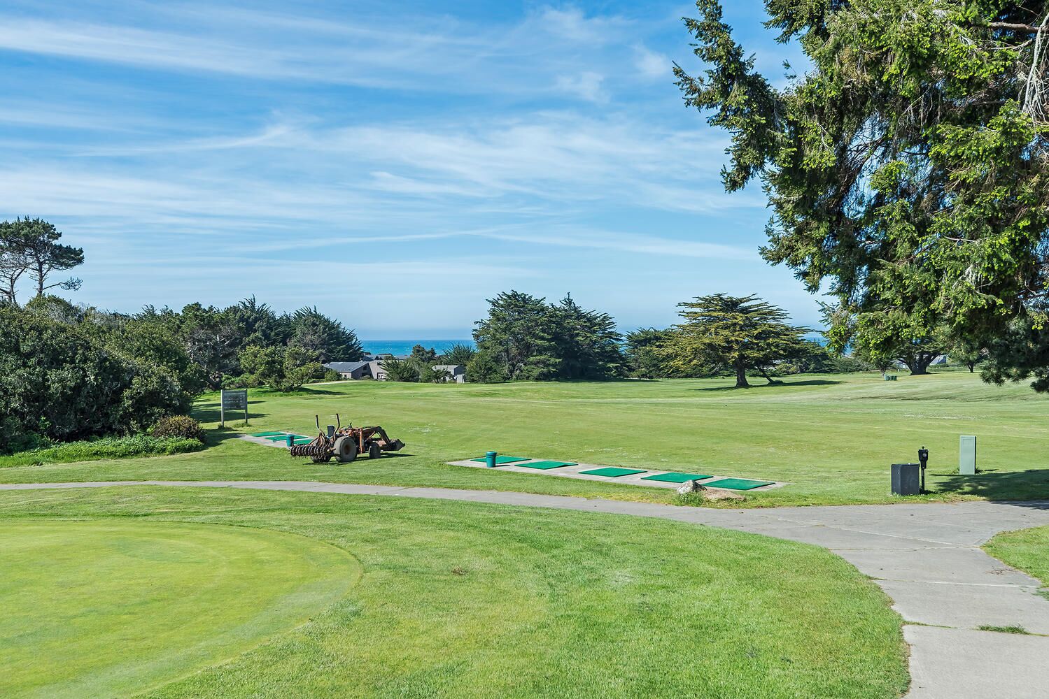 A golf course with a clear view of the ocean, a golf cart, and a well-maintained lawn.