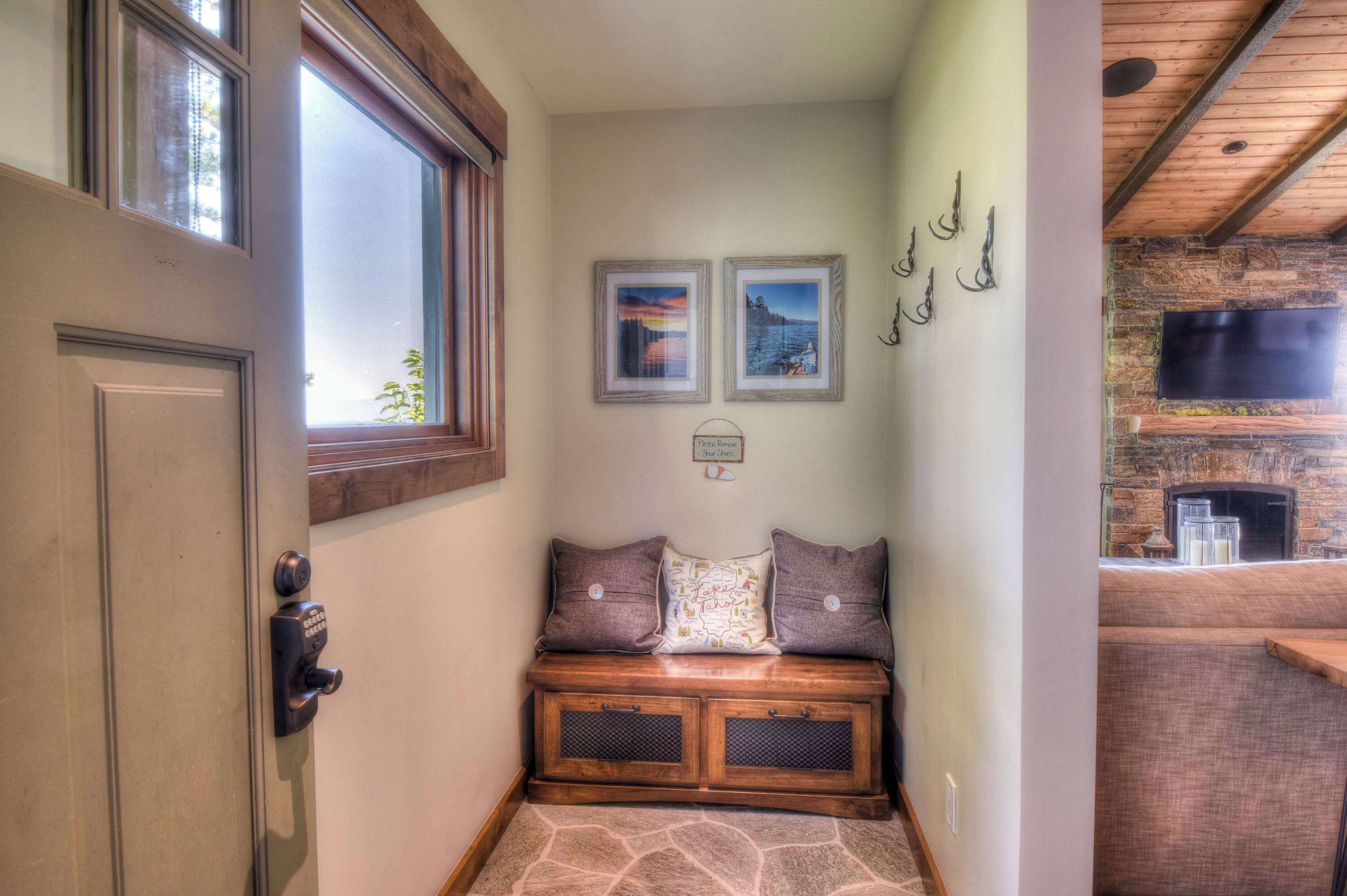 A hallway with a stone bench, a door with a keypad lock, and a fireplace with a TV above it.
