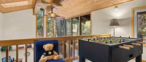Um quarto aconchegante com uma cadeira azul, um urso de pelúcia e uma mesa de pebolim.