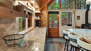 Una cocina moderna con encimera de mármol, armarios de madera y un amplio ventanal con vistas a un bosque.