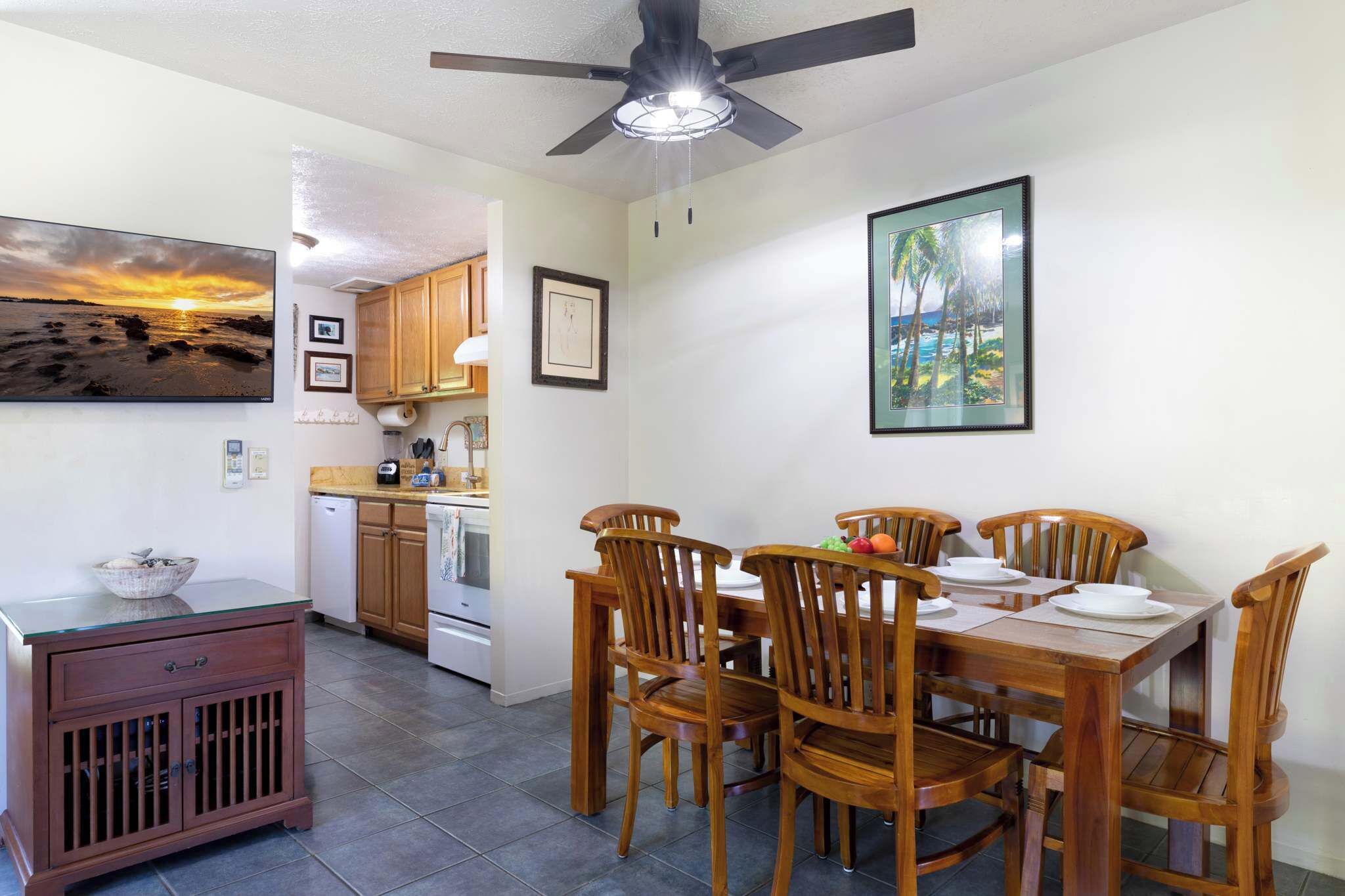 A dining area with wooden chairs and a table, a ceiling fan, and framed pictures on the walls.