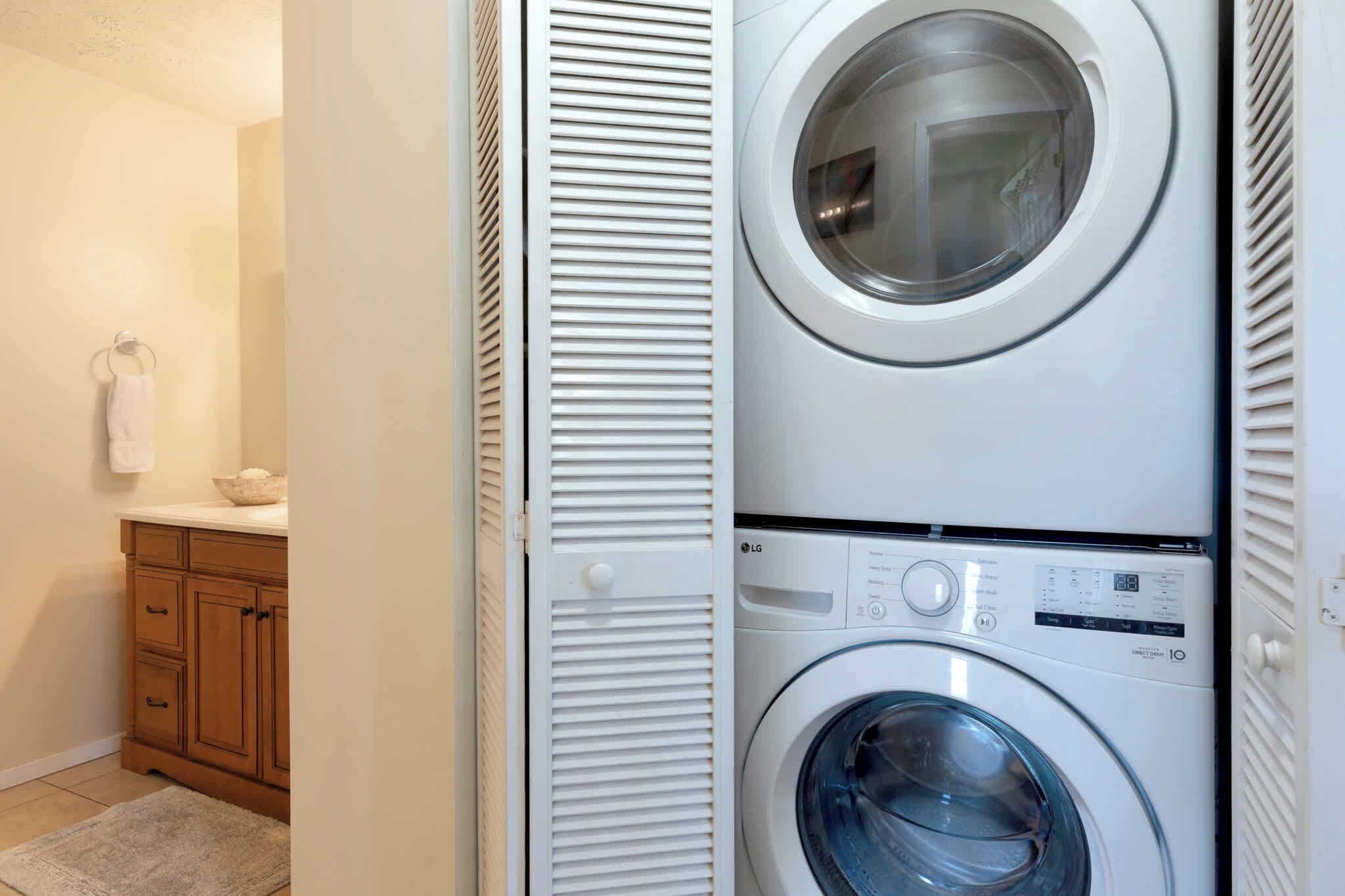 A laundry room with stacked washers and dryers, wooden cabinets, and a towel rack.