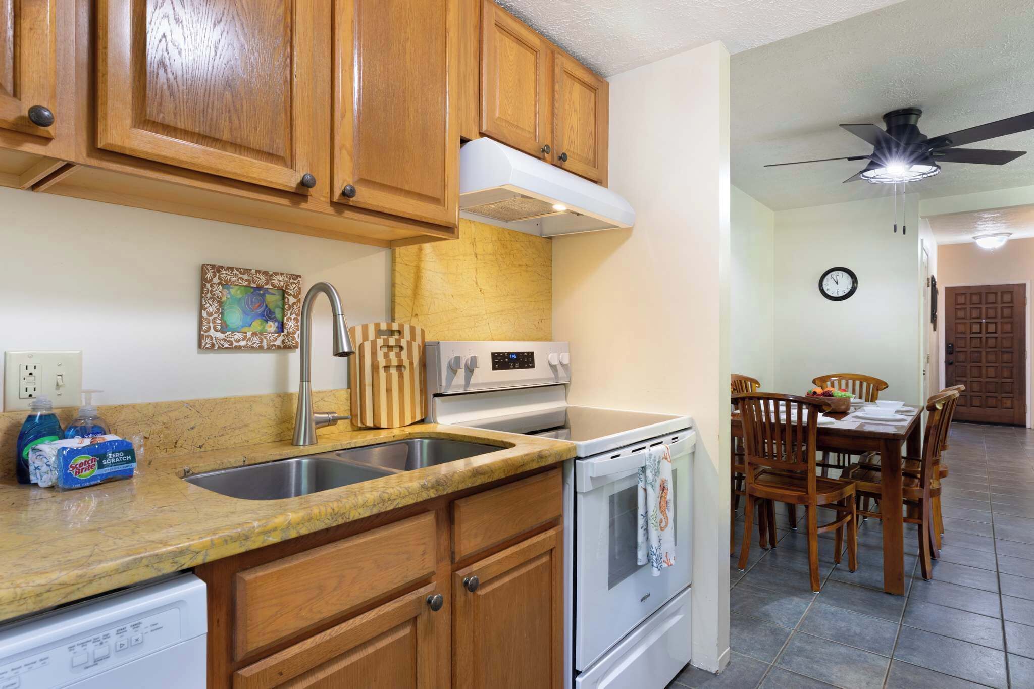 A kitchen with wooden cabinets, a stainless steel sink, a built-in oven, and a dining area with wooden chairs and a table.