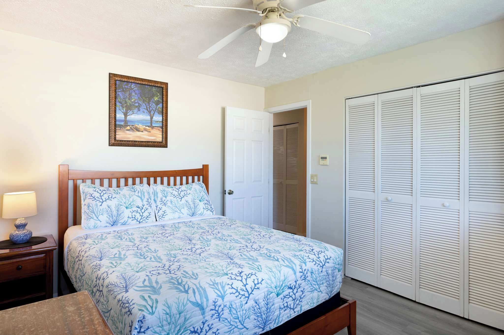 A bedroom with a bed, a ceiling fan, a nightstand, a lamp, a framed picture, a door, and a closet.