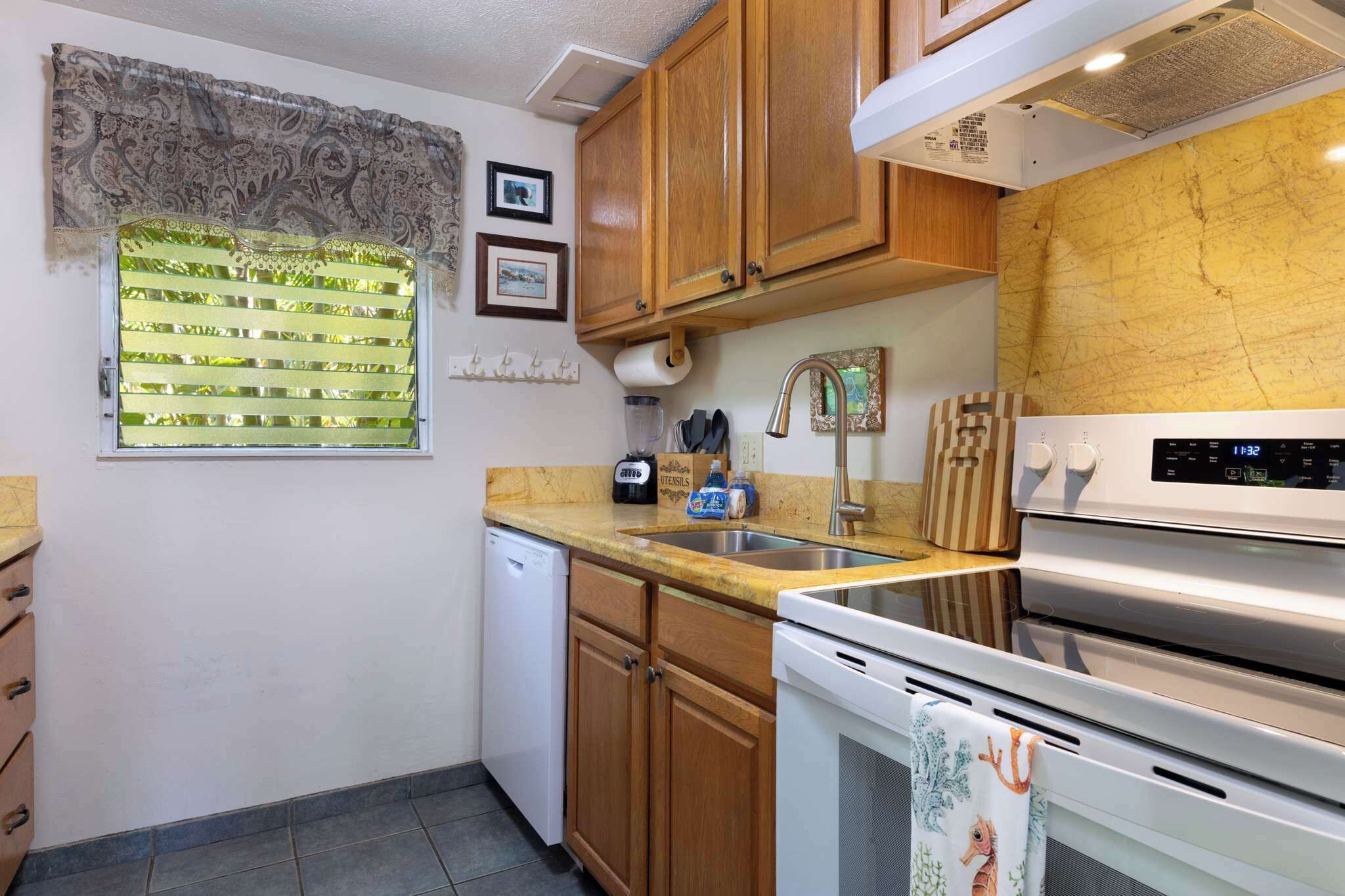 A kitchen with wooden cabinets, a stainless steel oven, a dishwasher, and a window with blinds.