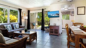 A spacious living area with a sofa, coffee table, and dining table set for four. - Surf & Racquet Club #24 New Beds, New You! (Kailua-Kona)