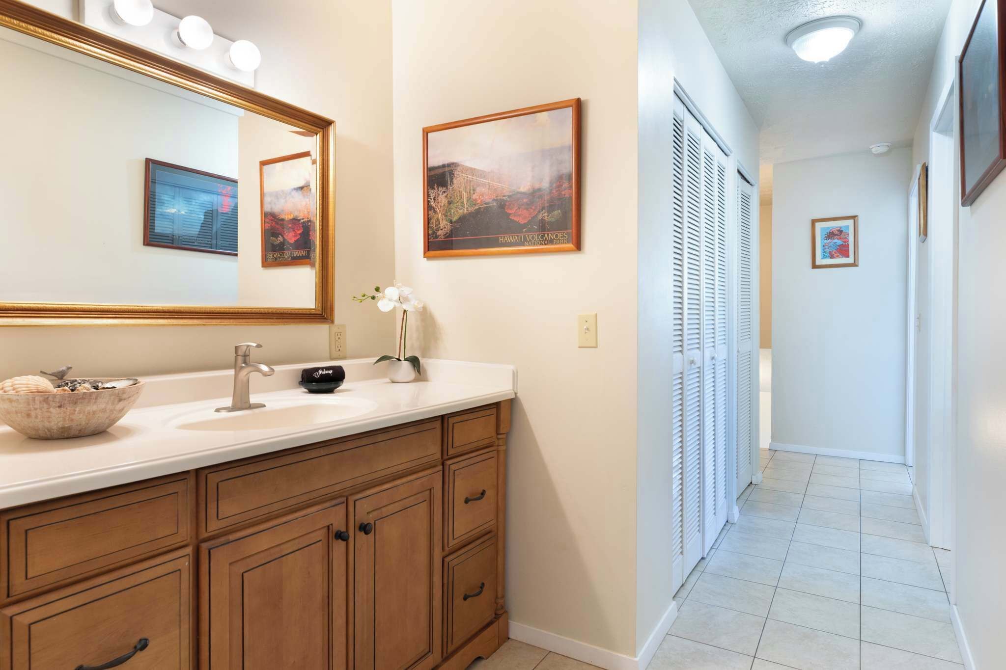 A bathroom with a large mirror, vanity, and a framed picture of Hawaii volcanoes.
