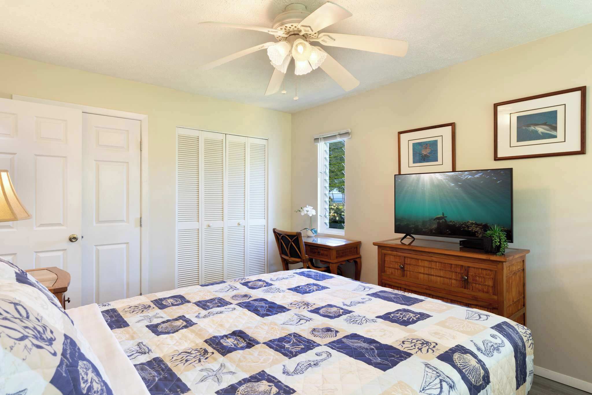 A bedroom with a bed, a ceiling fan, a television, and framed pictures on the wall.