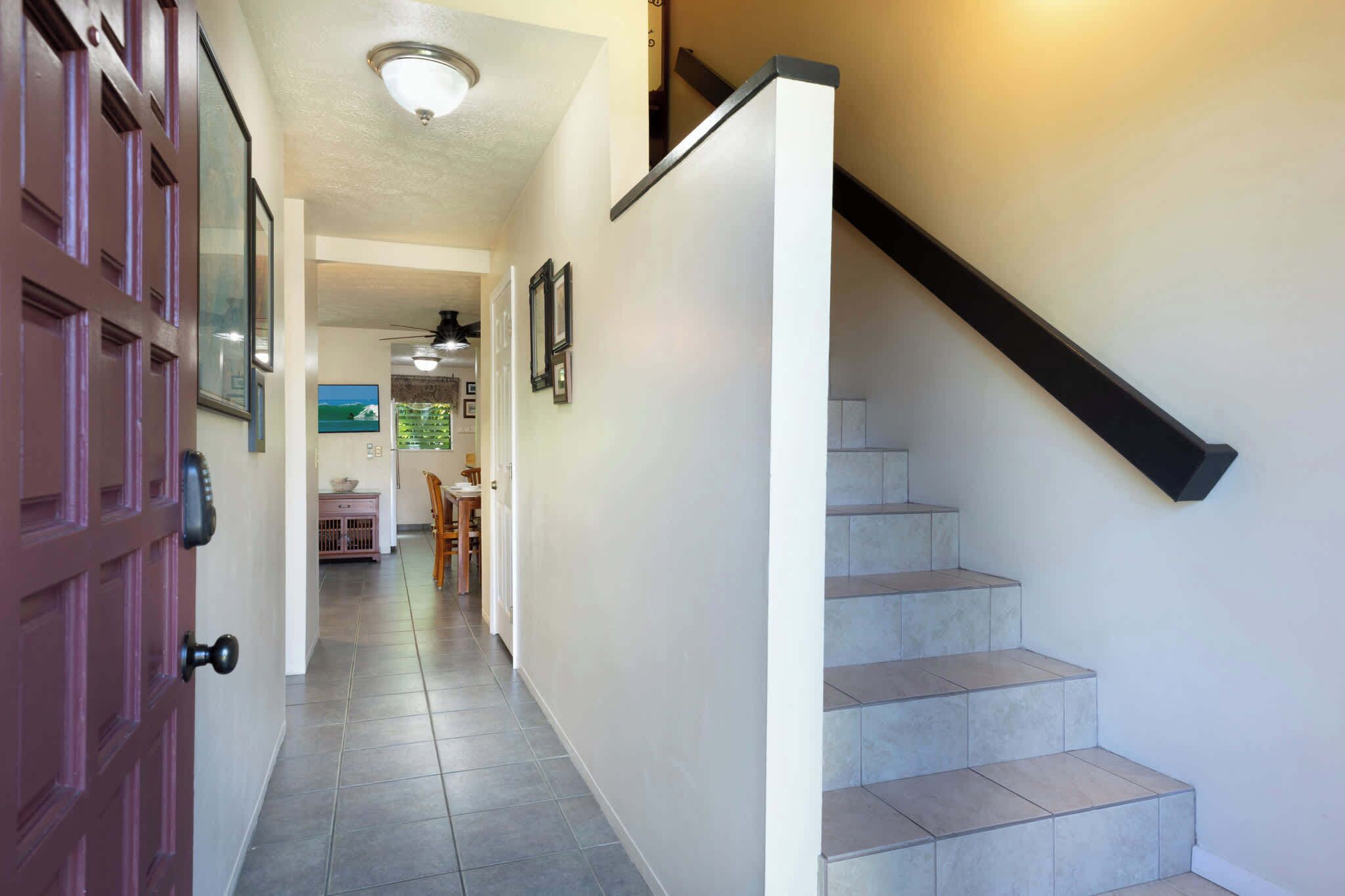 A hallway with a staircase, a door, and a ceiling fan.