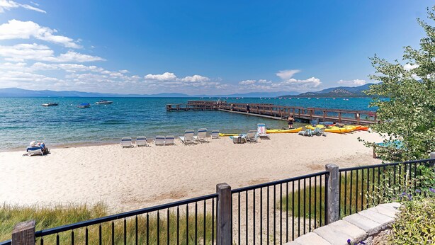 A beach with a wooden pier extending into the water, surrounded by lounge chairs and kayaks. - Whiskey Rock (South Lake Tahoe)