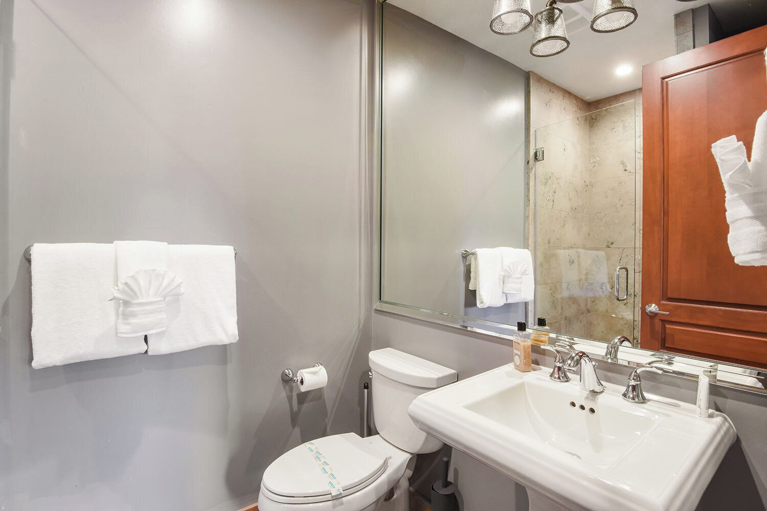 A bathroom with a toilet, sink, and mirror. There are towels hanging on the wall and a shower area visible in the background.