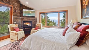 Ein Schlafzimmer mit Kamin aus Stein, einem großen Bett, zwei Sesseln und einem an der Wand montierten Fernseher.