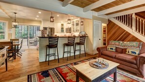 Un vaste espace de vie doté d’un plafond en bois, une cuisine avec un bar et un coin salon confortable avec un canapé et une table basse.