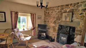 Una sala de estar con chimenea de piedra, televisor, mesa de comedor con sillas y ventana con cortinas.