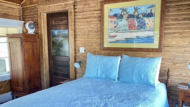 A bedroom with a wooden wall, a bed with a blue quilt, a wooden door, and a framed painting above the bed. - Cozy Cool Apartment on 6th Street!
WALK TO ACL FEST! (Austin)