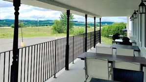 A covered outdoor area with tables and chairs, a railing, and a view of a green landscape. - Ramada by Wyndham Florenceville (Florenceville-Bristol)