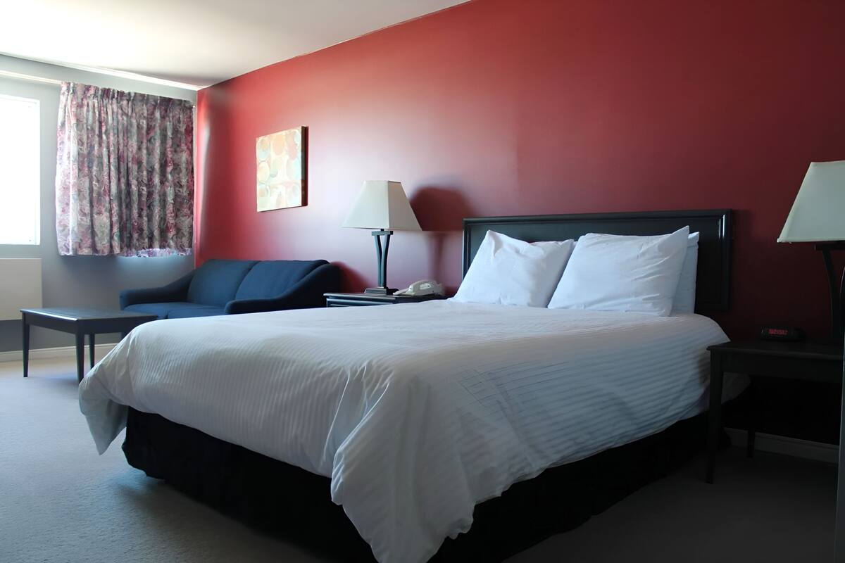 A hotel room with a large bed, a nightstand, a lamp, a chair, and a window with curtains.