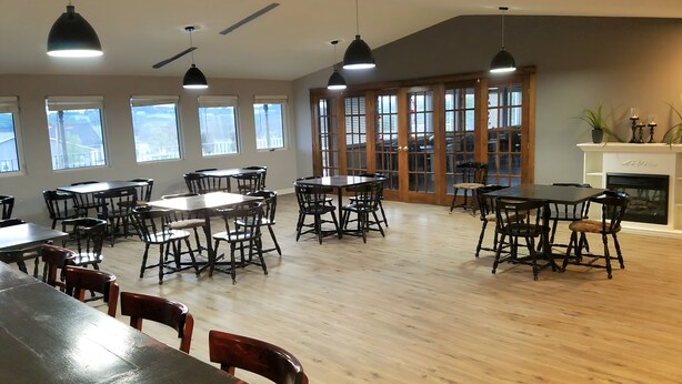A spacious dining area with multiple tables and chairs, large windows, and a fireplace. - Ramada by Wyndham Florenceville (Florenceville-Bristol)