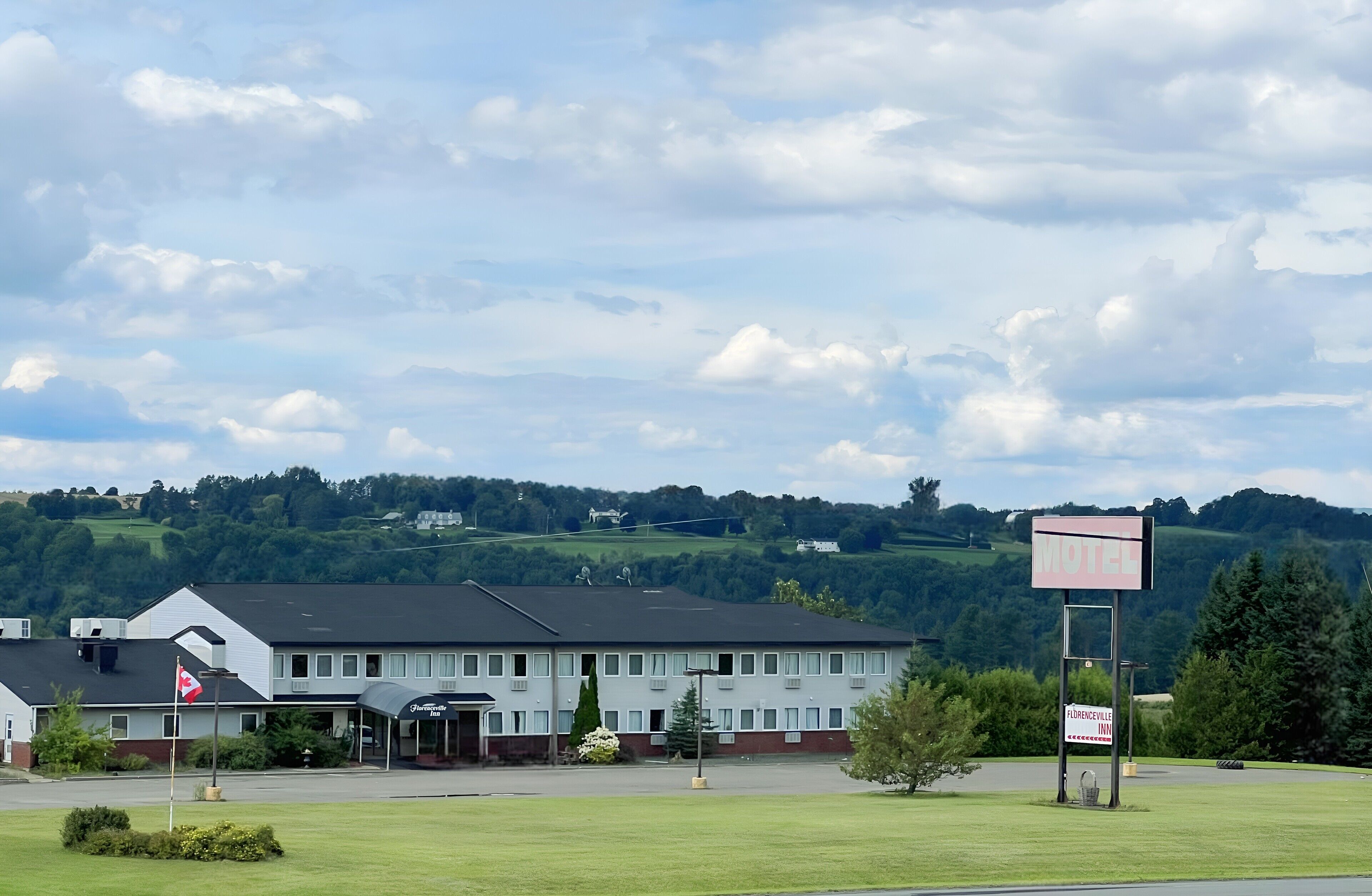 Ein Motel mit Schild, Flagge und einem Gebäude mit dunklem Dach und mehreren Fenstern.