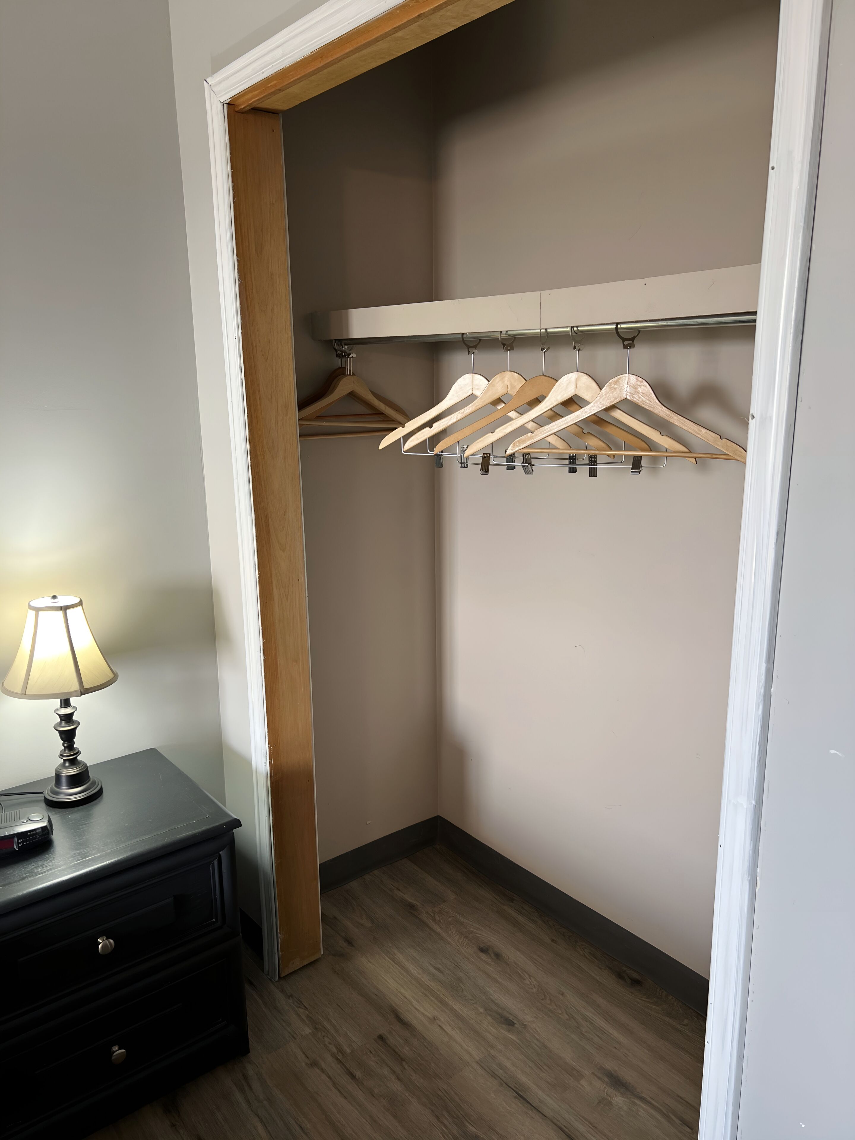 Un placard avec des cintres en bois et une lampe sur une commode.