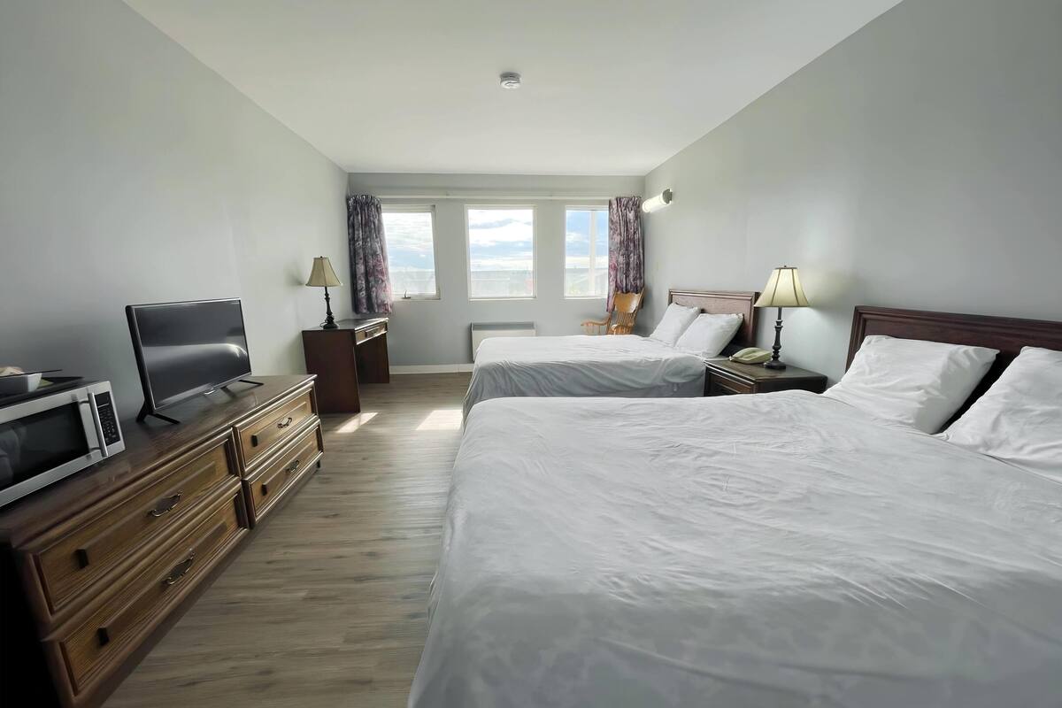 A hotel room with two beds, a TV, a desk, and a chair.