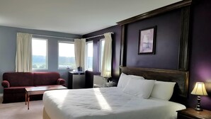 A hotel room with a large bed, a desk, a red sofa, and two windows with curtains. - Ramada by Wyndham Florenceville (Florenceville-Bristol)