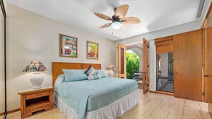 Un dormitorio con cama, mesitas de noche, ventilador de techo y puerta que da a un balcón.