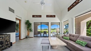 A spacious living area with a large flat-screen TV, a beige sofa with green cushions, a wooden coffee table, and a potted plant. - Exclusive Single-story Shores Golf Villa 20 - 3 Ensuite (Waikoloa)