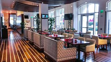A spacious restaurant with a long wooden floor, multiple seating areas, and large windows allowing natural light.