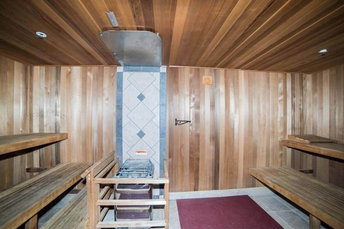 A sauna with wooden walls and benches, a central heating unit, and a tiled floor.